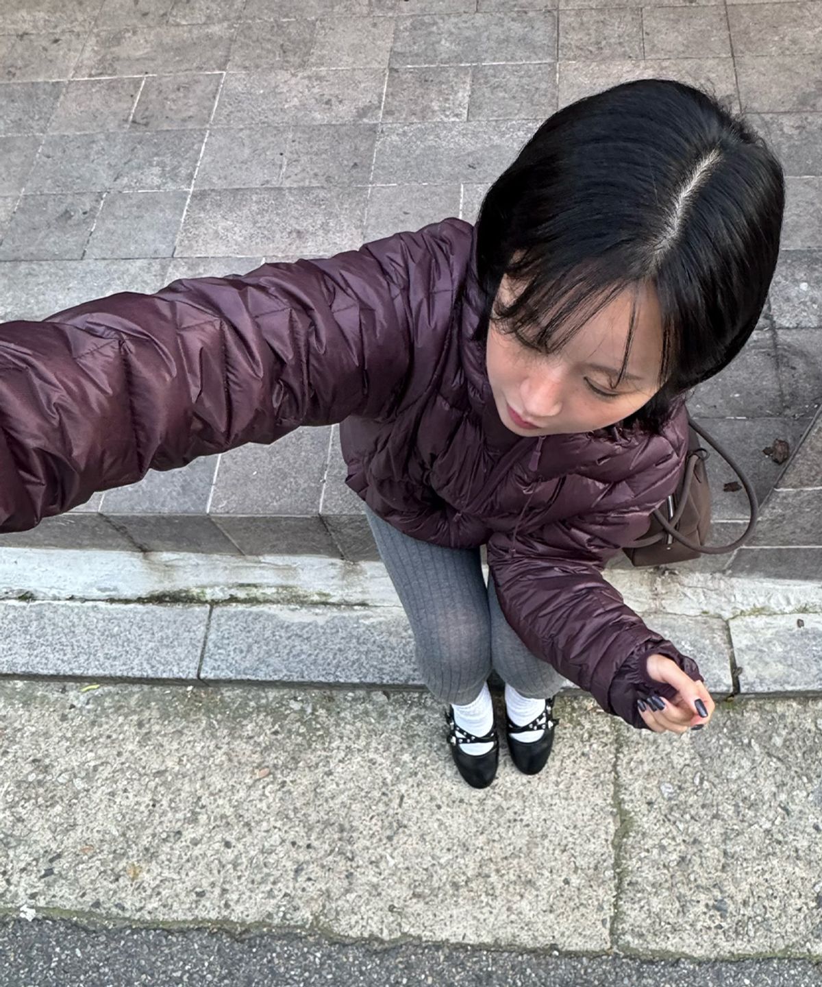 야외 카페 테라스에서 재킷을 입고 앉아 있는 모습으로 자연광 아래서의 블랙 컬러 광택감과 핏을 보여주는 사진