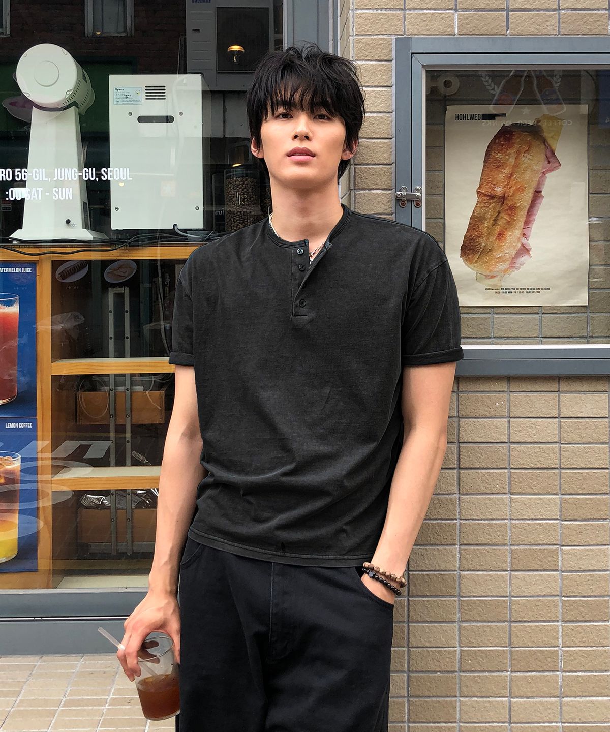 야외 카페 테라스에 앉아 있는 모습, 차콜 컬러 티셔츠와 베이지색 치노 팬츠가 잘 어우러진 가을 코디